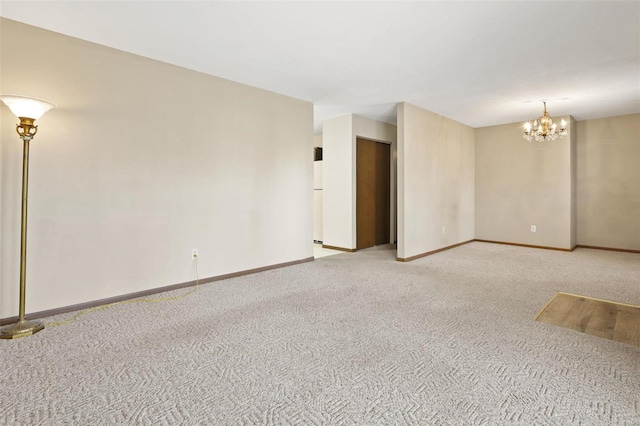 spare room with an inviting chandelier, carpet flooring, and baseboards