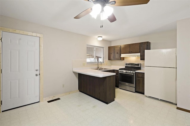 kitchen featuring a sink, under cabinet range hood, freestanding refrigerator, gas range, and light floors