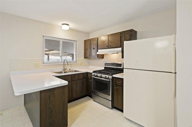 kitchen featuring under cabinet range hood, stainless steel range with gas stovetop, light floors, freestanding refrigerator, and a sink