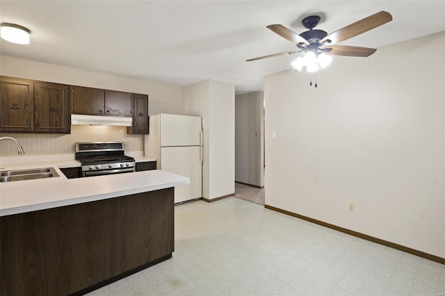 kitchen with under cabinet range hood, stainless steel range with gas stovetop, light countertops, freestanding refrigerator, and a sink