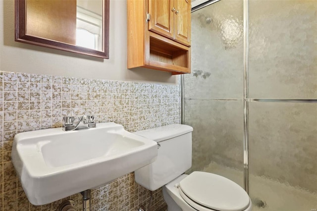 bathroom featuring a wainscoted wall, toilet, a stall shower, a sink, and tile walls