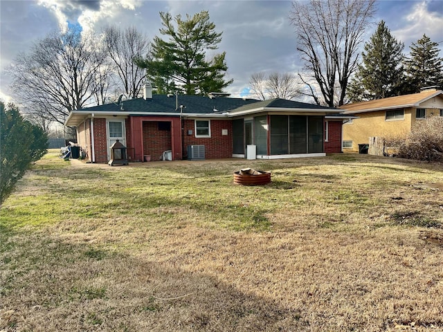 rear view of property with brick siding, a yard, an outdoor fire pit, a sunroom, and cooling unit