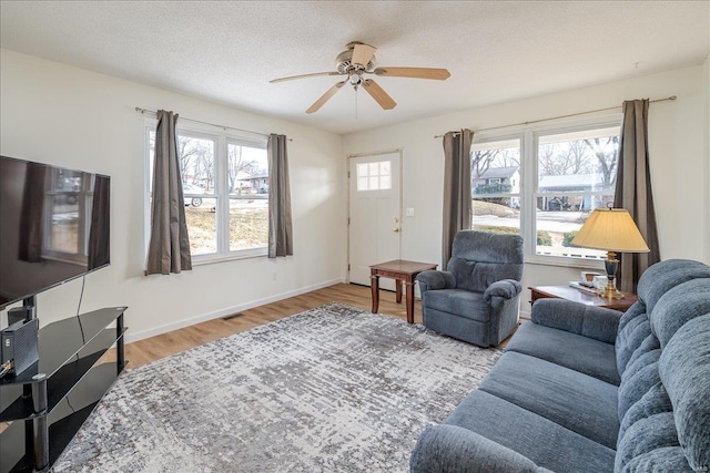 living room with a textured ceiling, a ceiling fan, baseboards, visible vents, and light wood-style floors