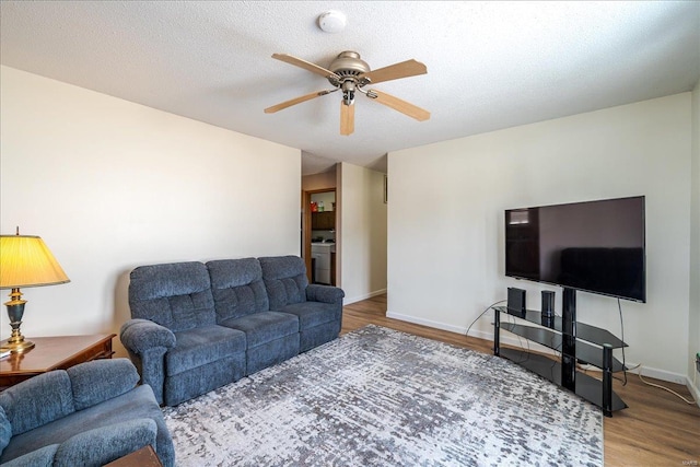 living room featuring a textured ceiling, wood finished floors, a ceiling fan, baseboards, and washer / clothes dryer