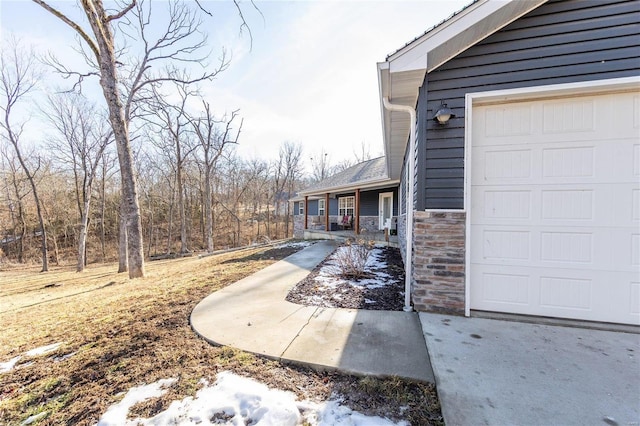 view of property exterior with a garage, stone siding, and covered porch