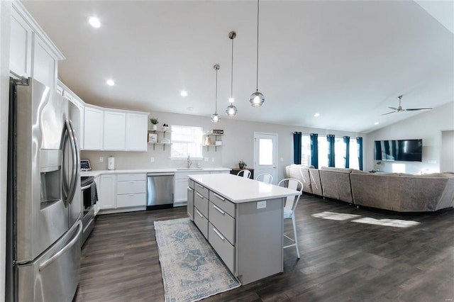 kitchen featuring open shelves, lofted ceiling, appliances with stainless steel finishes, a kitchen island, and a kitchen bar