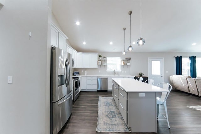 kitchen with stainless steel appliances, a sink, a center island, open shelves, and a kitchen bar