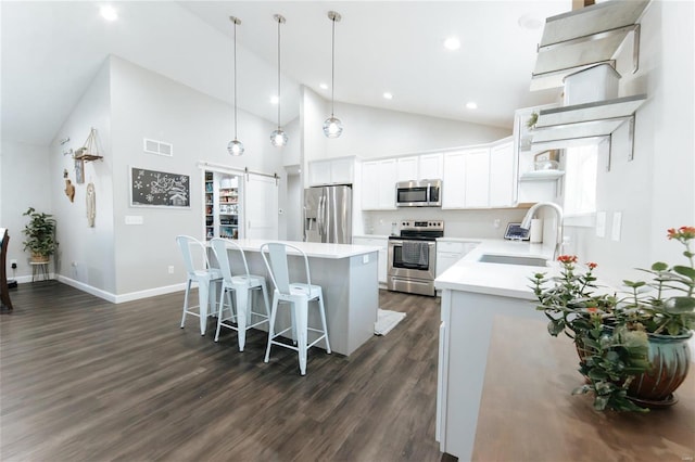 kitchen featuring a barn door, a kitchen island, appliances with stainless steel finishes, a kitchen breakfast bar, and a sink