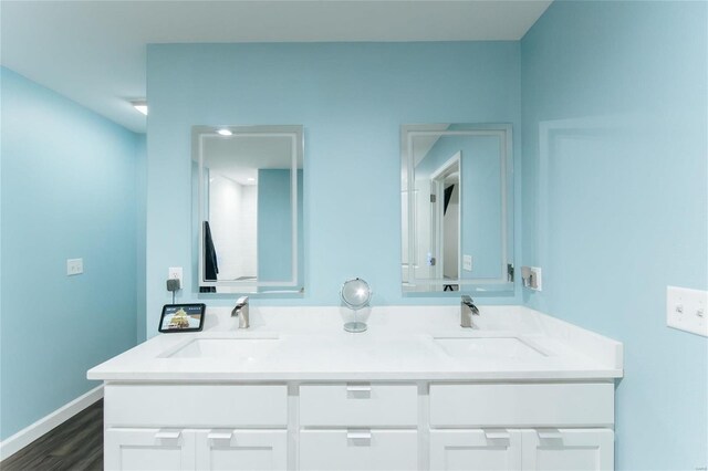 full bathroom featuring double vanity, baseboards, a sink, and wood finished floors