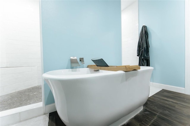 bathroom featuring a freestanding bath, baseboards, a tile shower, and wood finished floors