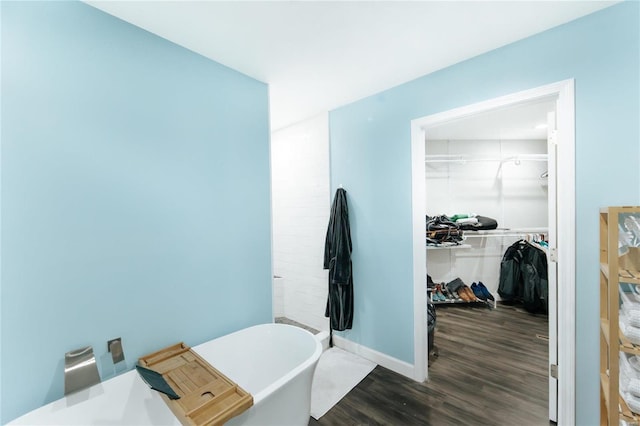 bathroom with a soaking tub, wood finished floors, a walk in closet, and baseboards