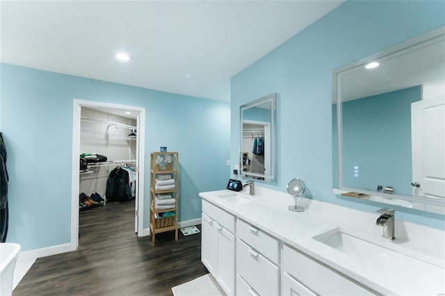 bathroom with a walk in closet, a sink, baseboards, and wood finished floors