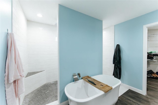 bathroom with a freestanding bath, a spacious closet, wood finished floors, baseboards, and walk in shower