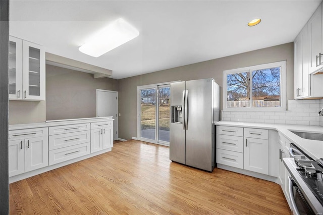 kitchen with light countertops, stainless steel refrigerator with ice dispenser, decorative backsplash, and light wood-style floors