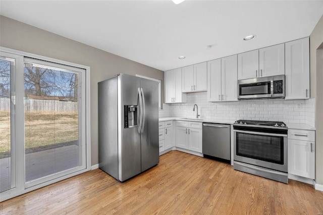 kitchen featuring light wood finished floors, tasteful backsplash, stainless steel appliances, and a sink