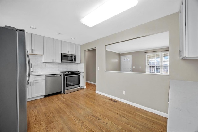 kitchen with light wood finished floors, baseboards, visible vents, stainless steel appliances, and backsplash