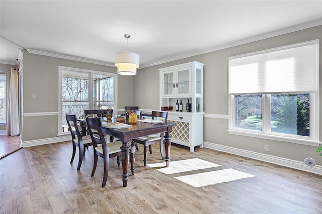 dining space with a healthy amount of sunlight, light wood-type flooring, baseboards, and crown molding