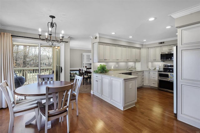 kitchen with decorative light fixtures, a peninsula, stainless steel appliances, light countertops, and a sink