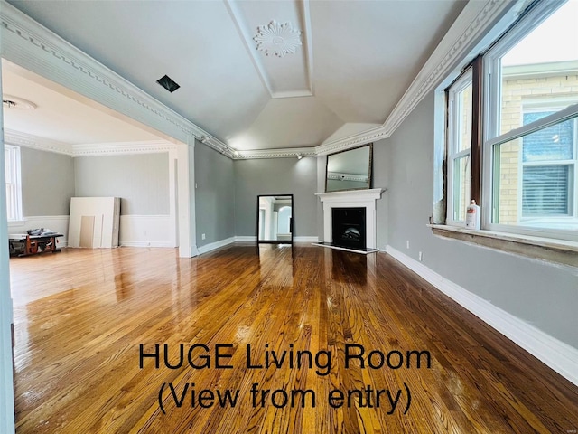 unfurnished living room featuring a fireplace with raised hearth, lofted ceiling, wood finished floors, baseboards, and crown molding