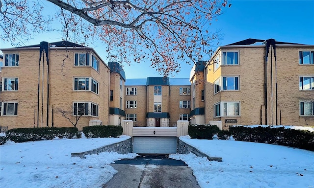 snow covered building featuring a garage and aphalt driveway