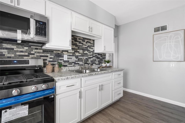 kitchen with stainless steel appliances, a sink, white cabinets, tasteful backsplash, and dark wood finished floors