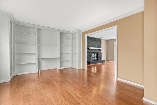 unfurnished living room featuring a brick fireplace, crown molding, baseboards, and wood finished floors