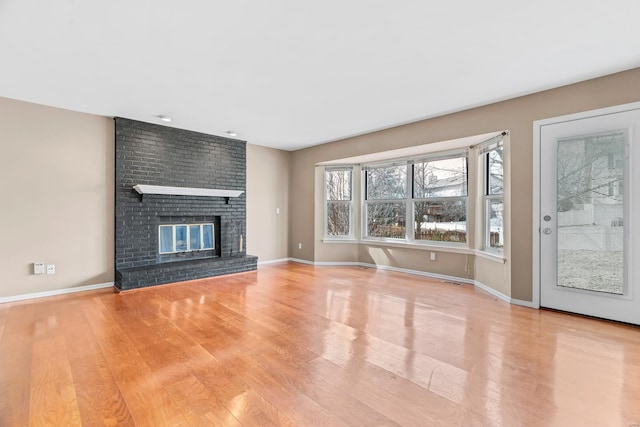 unfurnished living room featuring light wood-style floors, a brick fireplace, and baseboards