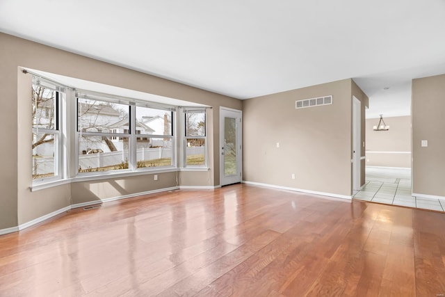 unfurnished room featuring light wood-style floors, baseboards, visible vents, and an inviting chandelier