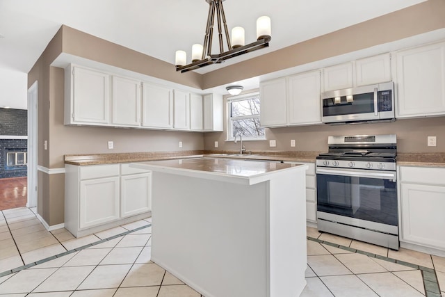 kitchen featuring decorative light fixtures, light countertops, appliances with stainless steel finishes, white cabinets, and a kitchen island