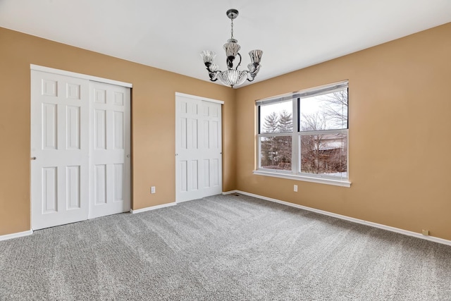 unfurnished bedroom featuring a notable chandelier, baseboards, carpet flooring, and multiple closets