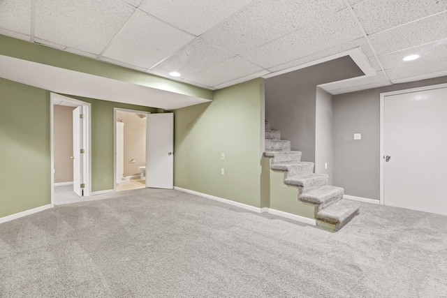 finished below grade area featuring stairs, carpet, a paneled ceiling, and baseboards