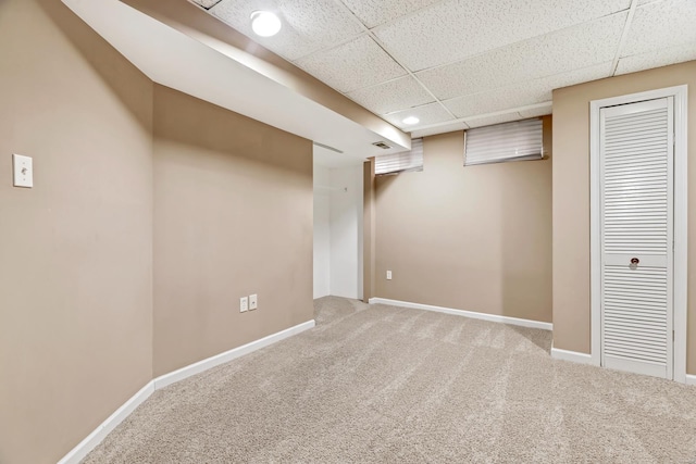 finished below grade area featuring a paneled ceiling, carpet flooring, and baseboards