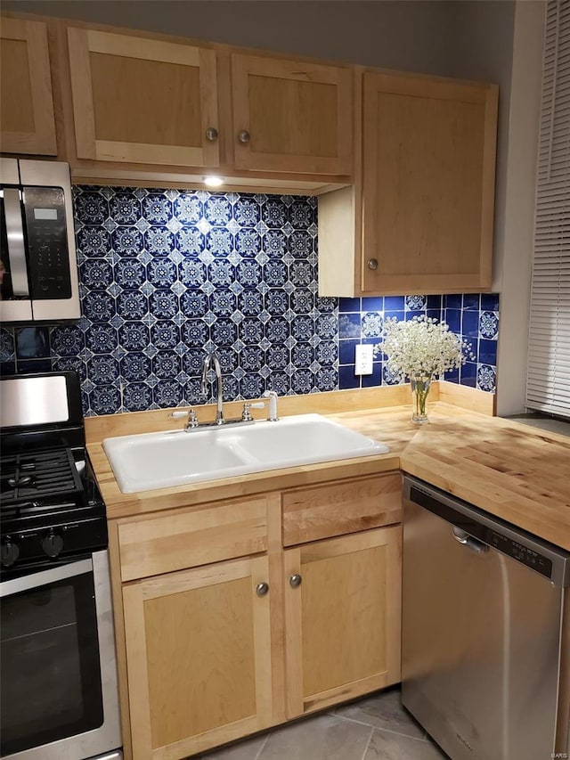 kitchen with appliances with stainless steel finishes, butcher block counters, a sink, and decorative backsplash