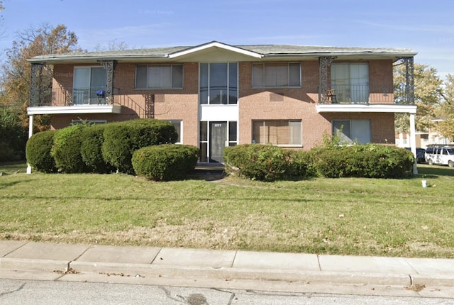 multi unit property with brick siding, a front yard, and a balcony