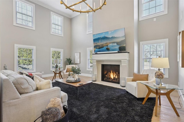 living area featuring light wood finished floors, baseboards, a lit fireplace, ornamental molding, and a notable chandelier