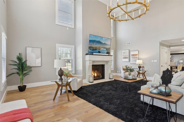 living room featuring visible vents, a fireplace with flush hearth, light wood-style floors, baseboards, and a towering ceiling