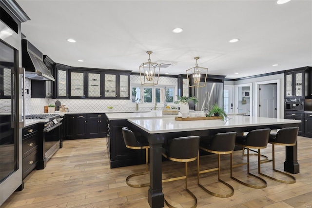 kitchen featuring a kitchen bar, wall chimney range hood, stainless steel range with gas stovetop, light countertops, and dark cabinets