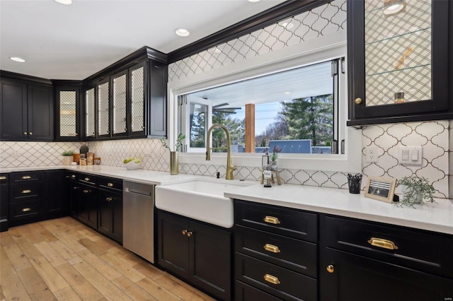 kitchen with dark cabinetry, a healthy amount of sunlight, a sink, glass insert cabinets, and stainless steel dishwasher