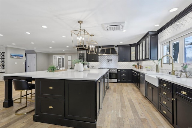 kitchen with a large island, a sink, dark cabinetry, appliances with stainless steel finishes, and wall chimney range hood