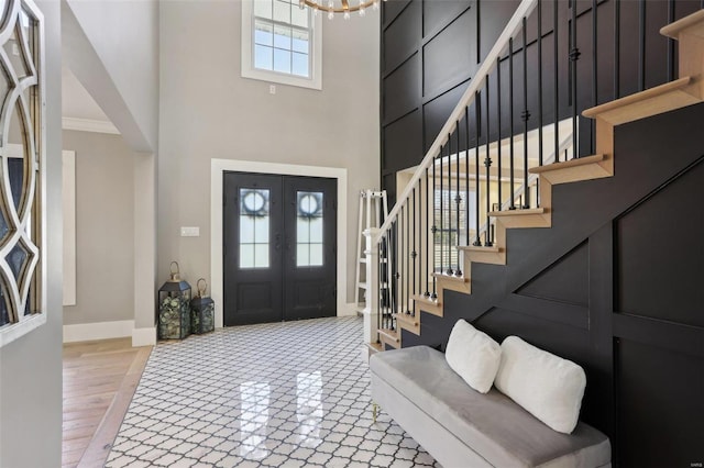 entrance foyer with stairway, baseboards, french doors, a towering ceiling, and a chandelier