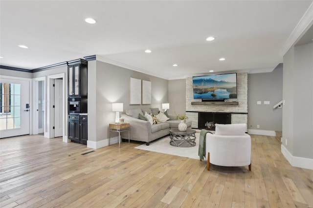 living area with light wood-style flooring, a fireplace, baseboards, and ornamental molding