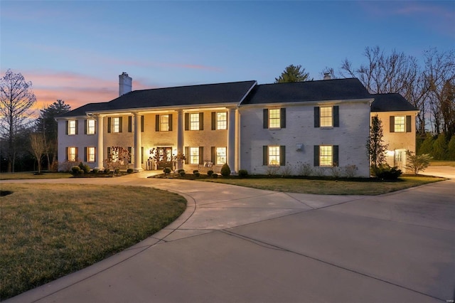 view of front facade with a porch, a lawn, driveway, and a chimney