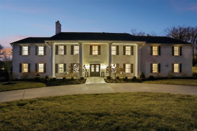 neoclassical / greek revival house featuring a porch, a chimney, and a front lawn