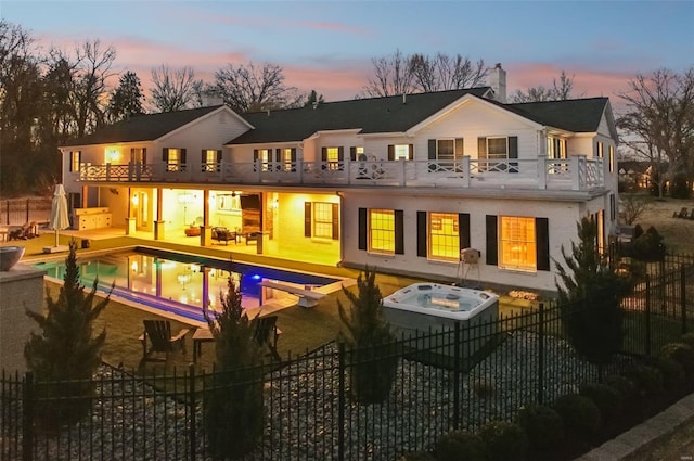 back of house at dusk with a balcony, an outdoor hot tub, fence private yard, and a fenced in pool