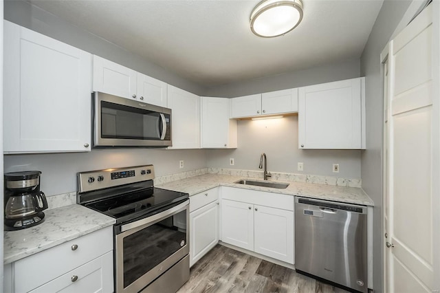 kitchen with stainless steel appliances, wood finished floors, a sink, white cabinetry, and light stone countertops