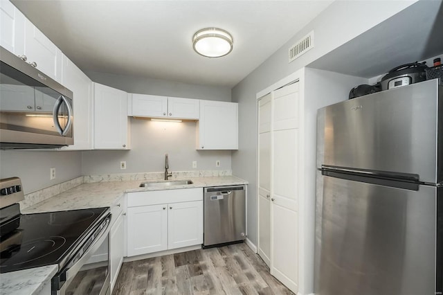 kitchen featuring light wood-style flooring, stainless steel appliances, a sink, visible vents, and white cabinets