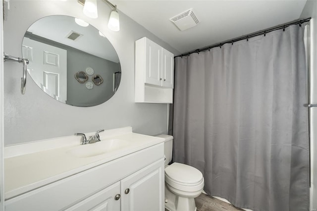 full bath featuring toilet, wood finished floors, vanity, and visible vents