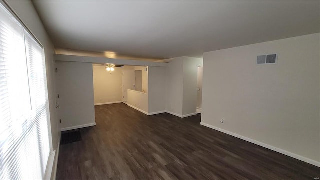 empty room with ceiling fan, dark wood-style flooring, visible vents, and baseboards