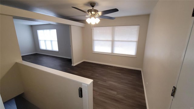 empty room featuring ceiling fan, dark wood-style flooring, and baseboards