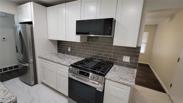 kitchen with light stone countertops, marble finish floor, white cabinetry, and stainless steel appliances